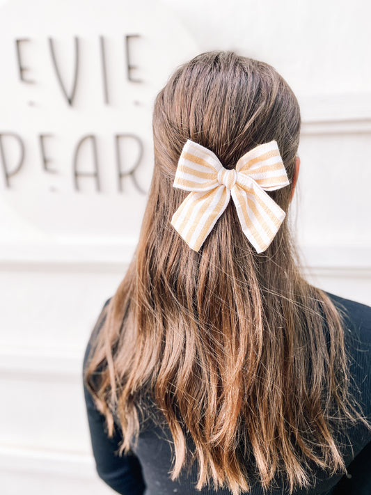 Girl wearing cream and yellow striped large pinwheel bow: fall neutral hair accessory for toddlers and girls